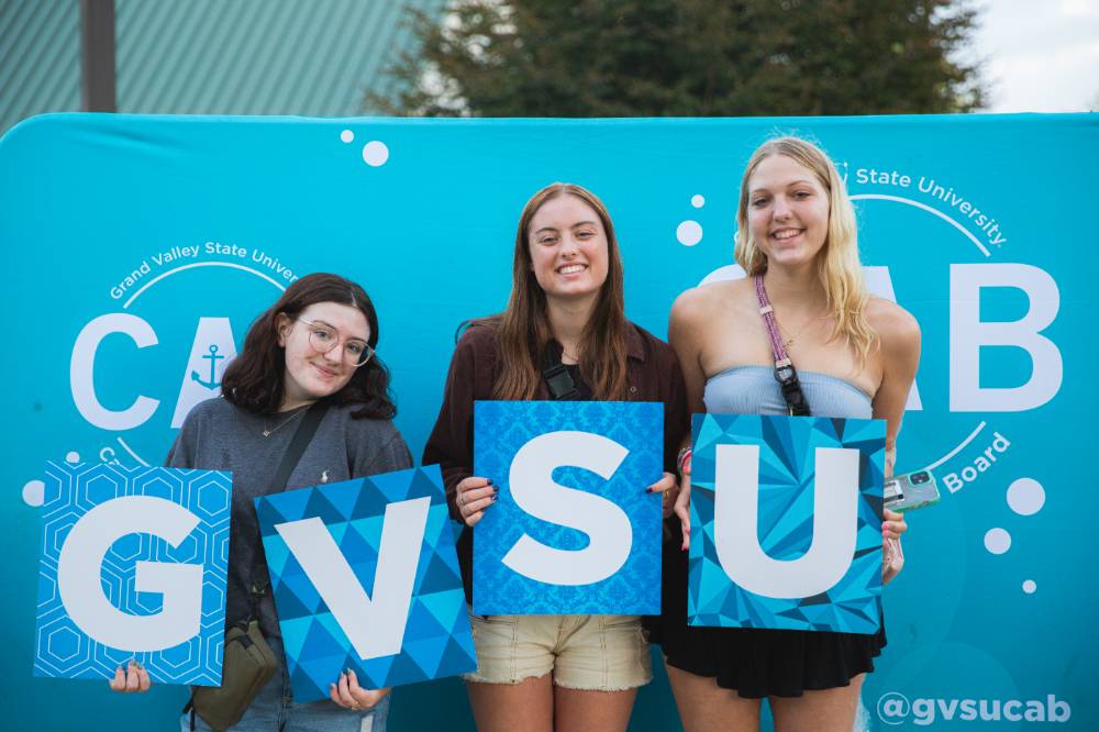three students posing in front of backdrop at Laker Kickoff photo booth holding GVSU letters